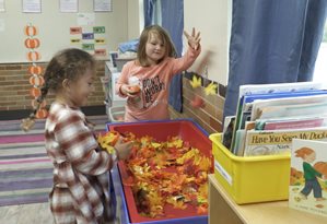 two preschool students playing with autumn leaves at an activity table